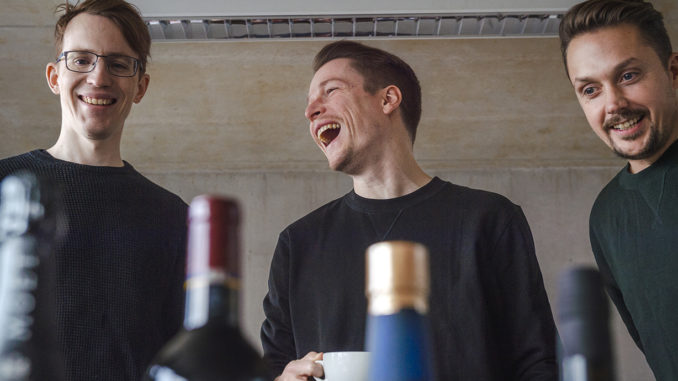 The three founders of spiritory laughing - Janis Wilczura, alumnus of Munich Business School in the middle; bottle tops in foreground