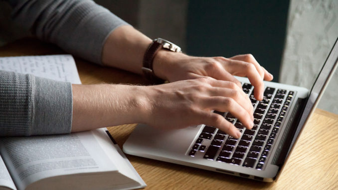 Close up of man typing his thesis on laptop