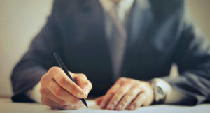 EMBA vs MBA: Close up of hands of man holding pen and writing.