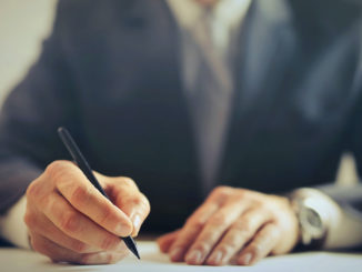 EMBA vs MBA: Close up of hands of man holding pen and writing.