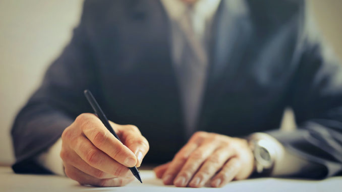 EMBA vs MBA: Close up of hands of man holding pen and writing.