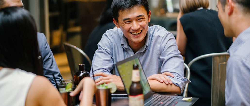 A group of young and energetic Asian co-workers sit around a table and have a light hearted business discussion and drinking beer..