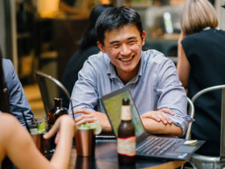 A group of young and energetic Asian co-workers sit around a table and have a light hearted business discussion and drinking beer..