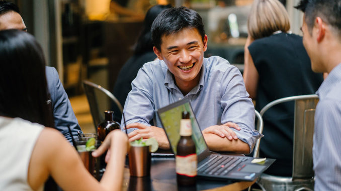 A group of young and energetic Asian co-workers sit around a table and have a light hearted business discussion and drinking beer..