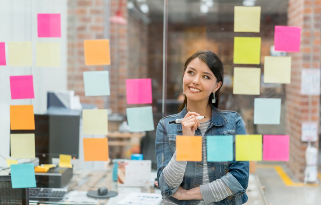 Young woman in front of a glass pane with many colorful post-its organizing a project