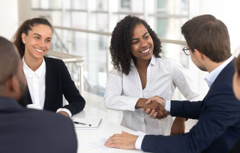 Woman and man shaking hands in a group meeting to welcome a new employee