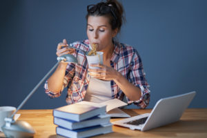 Food for the brain: Female student eating Asian noodles while learning at home