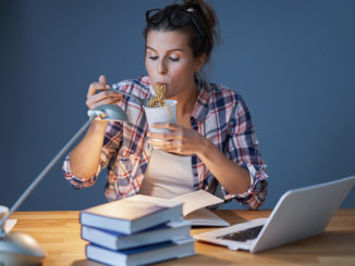 Food for the brain: Female student eating Asian noodles while learning at home