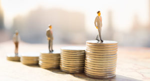 Miniature figures standing on stacks of coins of different heights