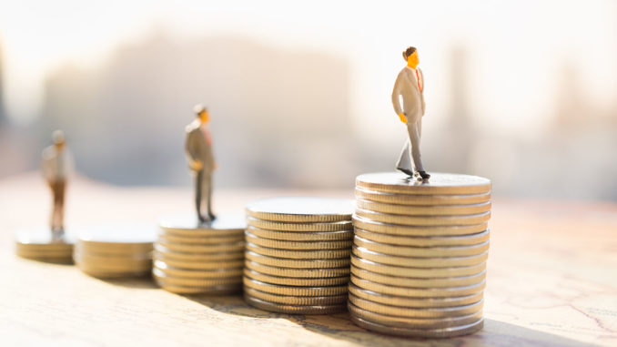 Miniature figures standing on stacks of coins of different heights