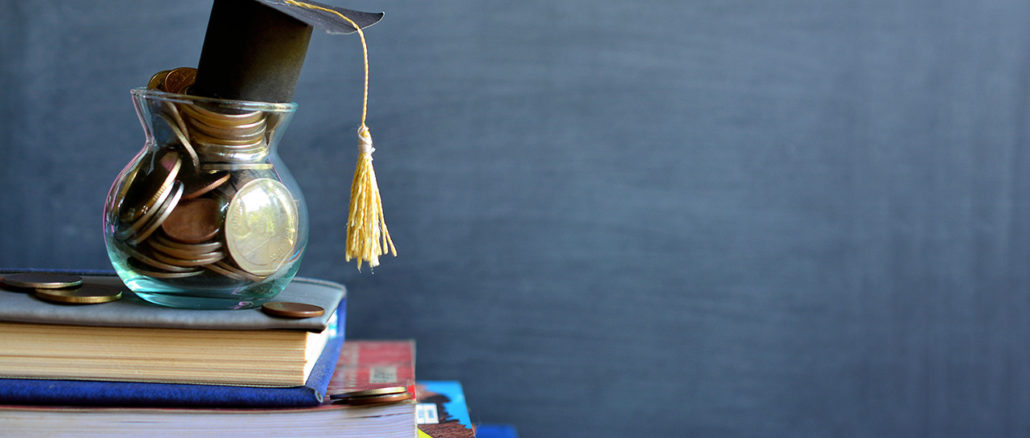 Concept of student financing: Graduation hat model on coins in a glass container on a stack of books