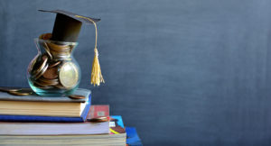 Concept of student financing: Graduation hat model on coins in a glass container on a stack of books