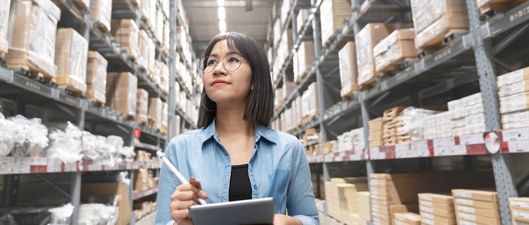 Young Asian Supply Chain Manager with a tablet in her hand walking through the warehouse.