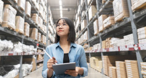 Young Asian Supply Chain Manager with a tablet in her hand walking through the warehouse.