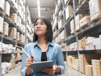 Young Asian Supply Chain Manager with a tablet in her hand walking through the warehouse.