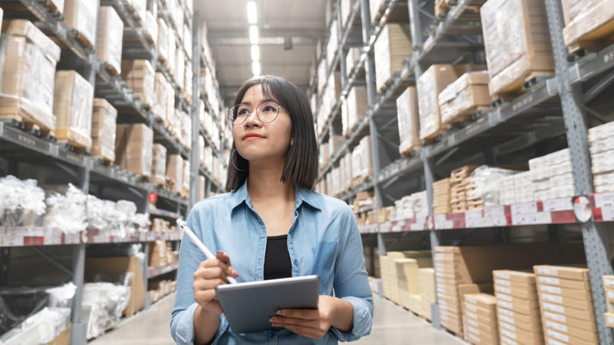 Young Asian Supply Chain Manager with a tablet in her hand walking through the warehouse.