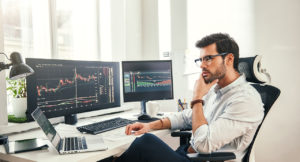 Young controller analyzing tables and graphs in front of several screens