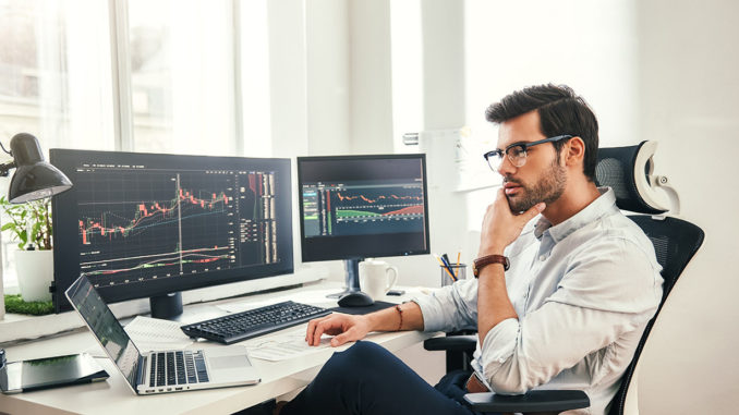 Young controller analyzing tables and graphs in front of several screens