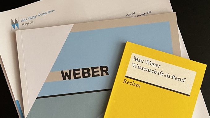 Top view of documents on the Max Weber Program, onto which Lucas Reischl, student of Munich Business School was accepted: Certificate of Admission, Reclam booklet by Max Weber "Wissenschaft als Beruf".