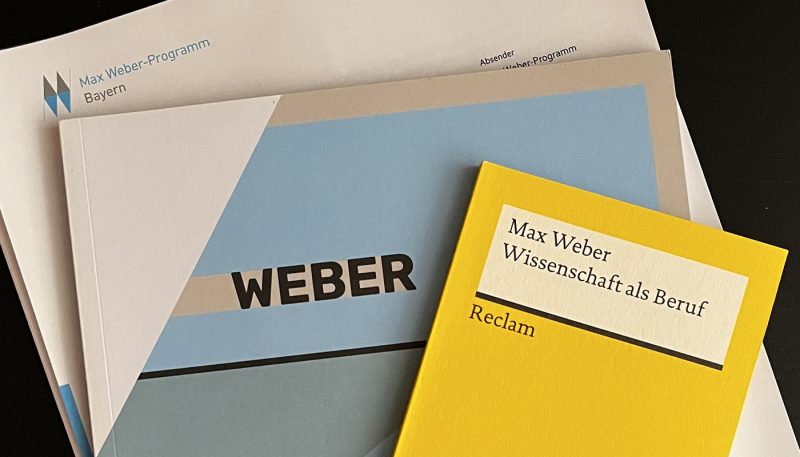 Top view of documents on the Max Weber Program, onto which Lucas Reischl, student of Munich Business School was accepted: Certificate of Admission, Reclam booklet by Max Weber 