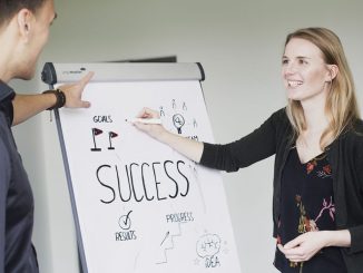 Two students from Munich Business School standing together at a flipchart with "success" written on it, representing a typical practical work situation at private universities.